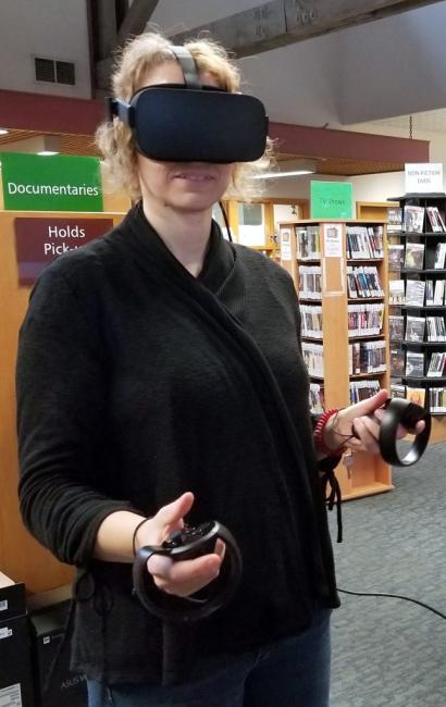 A woman with a VR headset and controls on her hands. The background is a library.