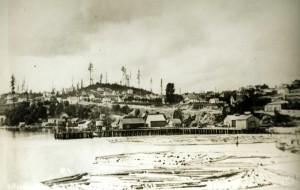 State Library Photograph CollectionAR-07809001-ph002112Photo showing Seattle in 1874, with logs floating in water, dock, buildings, hill, and trees